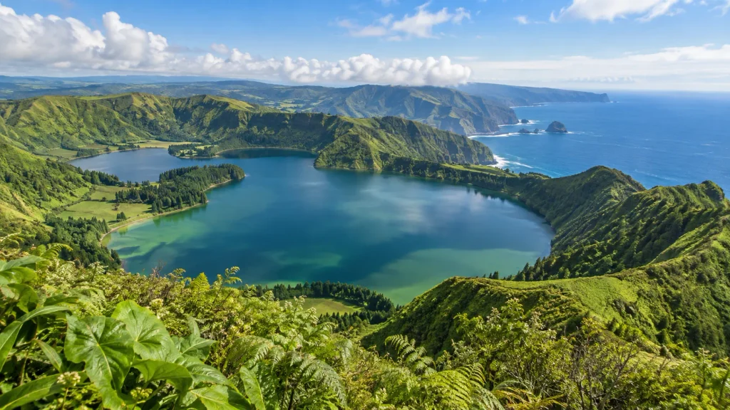 Grüner Vulkansee auf São Miguel auf den Azoren mit bewaldeten Kraterhängen und Atlantikküste