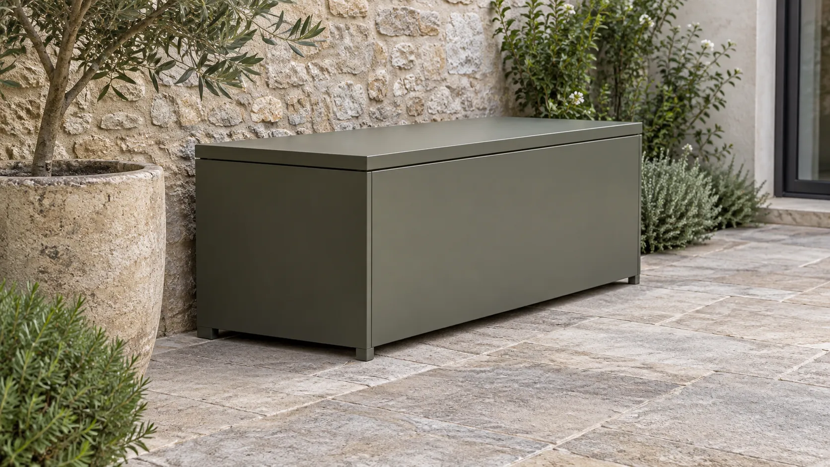 Olivgraue Metall-Auflagenbox auf Steinplatten neben einer Natursteinwand.